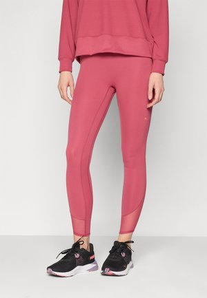Roze atletske tajice s glatkom teksturom i prilagođenim dizajnom, uparenih s crnim tenisicama za trčanje koje imaju uzorak u ružičastoj boji.