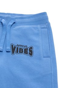 Pantaloni della tuta azzurro chiaro con vita elasticizzata e cordino. Presenta una grafica nera "AWESOME VIBES" sulla coscia sinistra e tasche laterali.