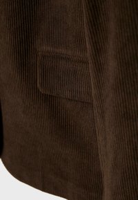 Gros plan sur une poche de veste en velours côtelé marron foncé avec une texture rainurée verticale visible et des détails de couture.