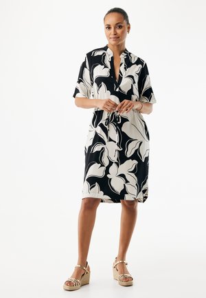 Czarna i biała sukienka w kwiaty z krótkimi rękawami, kołnierzem i paskiem w talii. Gładka tkanina, długość do kolan. Noszona z sandałami na koturnie.