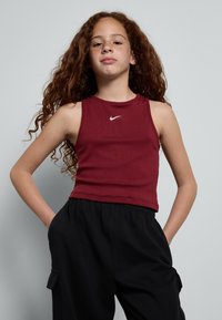 Bordo brezrokavnik z rebrasto teksturo in belim Nike logotipom. V kombinaciji s črnimi hlačami sproščenega kroja z stranskimi žepi.