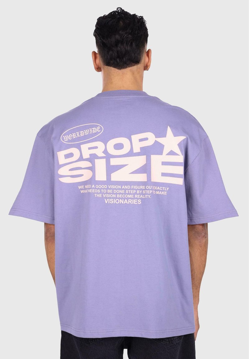 Lilla bomull t-skjorte med korte ermer. Har stor hvit tekst bak, inkludert "DROP SIZE" og en stjernegrafikk.