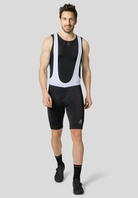 Bretelles de cyclisme noires sans manches avec culotte rembourrée. Comprend un haut en maille texturée et des chaussures de cyclisme noires.