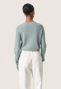 Top a maniche lunghe rigato blu chiaro, con scollatura rotonda. Abbinato a pantaloni bianchi texturizzati, con tasche posteriori e una leggera svasatura.