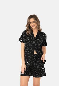 Czarny zestaw piżamowy z krótkim rękawem z wzorem białych owieczek. Bluzka zapinana na guziki, a szorty mają kieszenie dla dodatkowej wygody.