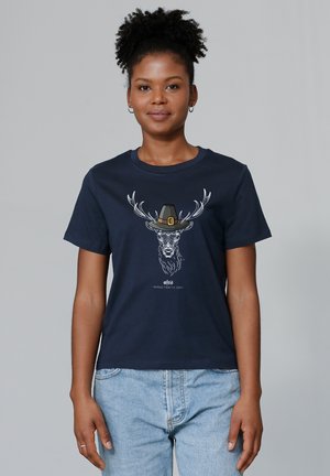 T-shirt en coton navy affichant un graphique d'un cerf avec des bois portant un chapeau. Manches courtes, col rond et coupe décontractée.