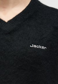 Μαύρο χνουδωτό πουλόβερ με λαιμόκοψη V, με λευκή κεντητή επιγραφή "Jacker" στο στήθος.