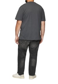 T-shirt en coton gris à manches courtes, associé à un jean en denim foncé avec un effet dégradé et un léger aspect usé, ainsi qu'une paire de baskets blanches.
