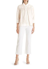 Helles rosa, strukturiertes Blusenshirt mit spitzem Kragen, Knopfleiste vorne und Dreiviertelärmeln. Kombiniert mit weißen, verkürzten Hosen und Riemchen-Heels.