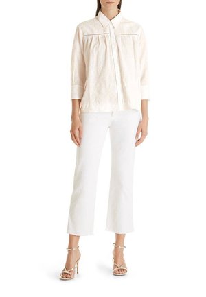 Vaaleanpunainen, teksturoitu pusero, jossa on terävä kaulus, nappilista edessä ja kolmivartiset hihat. Yhdistetty valkoisiin lyhyisiin housuihin ja remmikenkien kanssa.