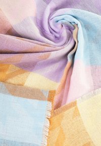 Couverture tissée légère aux couleurs pastel, avec un motif géométrique, des textures douces et des bords à franges.