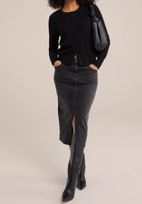 Svart stickad cardigan med knappar, i kombination med en grå denimkjol med en slits, och knähöga svarta stövlar med spetsig tå.