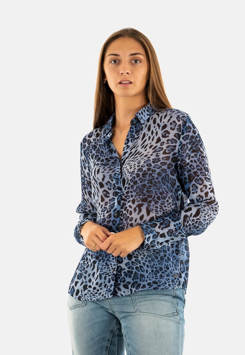 Blauwe luipaardprint overhemddas in lichte stof met lange mouwen, voorzien van een klassieke kraag en zwarte accenten. G gedragen met lichtblauwe jeans.