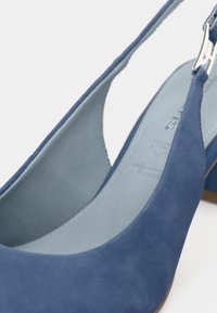 Escarpin bleu en daim avec un bout rond, doublure intérieure grise et une bride ajustable en métal argenté. Talon bas avec une finition lisse.