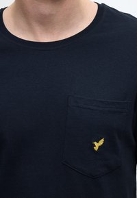 T-shirt in cotone blu navy con scollo tondo, caratterizzata da una tasca sul petto decorata con un piccolo logo ricamato a forma di uccellino giallo.