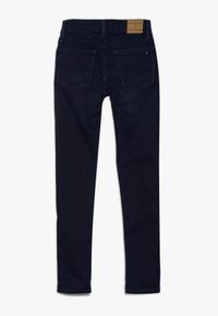 Jeans de mezclilla elástica de color azul oscuro, con un ajuste slim, diseño de cinco bolsillos, costuras visibles y una etiqueta de cuero marrón en la parte trasera de la cintura.
