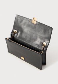 Sac à main en cuir noir au design épuré, avec un fermoir à rabat, des accessoires en métal doré, une anse en chaîne métallique et une poche intérieure zippée.