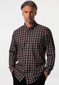 Camisa de cuadros en negro y rojo con mangas largas, cuello abotonado y botones blancos. Presenta un corte relajado con un bolsillo en el pecho.