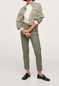 Veste aviateur à carreaux marron et blanc, associée à un pantalon ajusté à carreaux verts et des mocassins noirs avec un accent doré.