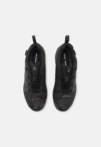 Black athletic shoes with a textured mesh upper, reinforced toe cap, elastic laces, and a pull tab at the heel for easy wear.
