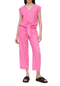 Roze linnen twee-delig outfit met een strik in de taille, korte mouwen en cropped wijde broekspijpen, gecombineerd met zwarte sandaaltjes met bandjes.