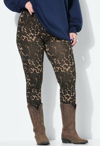 Leggings con stampa leopardo nelle tonalità di marrone e nero, abbinati a stivali da cowboy marroni. I leggings hanno una texture liscia e elasticizzata.