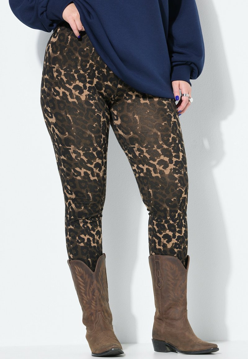 Leggings con stampa leopardo nelle tonalità di marrone e nero, abbinati a stivali da cowboy marroni. I leggings hanno una texture liscia e elasticizzata.