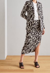 Ensemble composé d'un blazer et d'une jupe à imprimé léopard noir et blanc, avec une coupe ajustée, un tissu lisse et une fente sur le côté de la jupe. Porté avec des chaussures noires à enfiler.