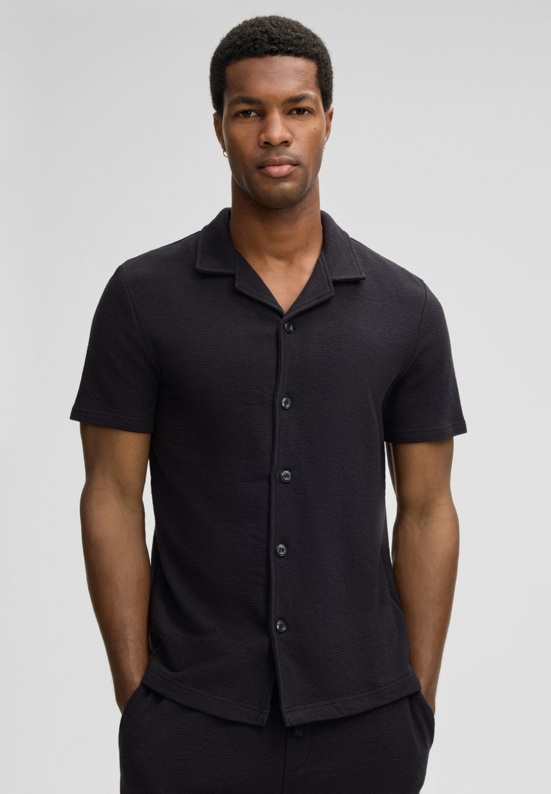Schwarzes Kurzarmhemd mit strukturierter Oberfläche, mit Knopfverschluss vorne, klassischem Kragen und lässiger Passform.