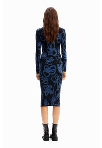 Niebieska sukienka dzianinowa w wzory, z długimi rękawami, dopasowanym krojem i prążkową strukturą, zestawiona z czarnymi masywnymi butami.