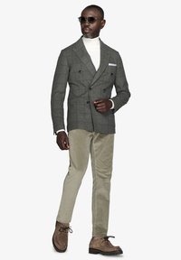 Gråternet dobbeltrækket blazer over en hvid rullekrave, parret med lysegrønne kordfløjspants og brune ruskinds sko.