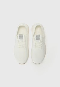 White athletic shoes with a textured knit upper, lace-up design, and a rubber sole. Features a small gray logo on each tongue.