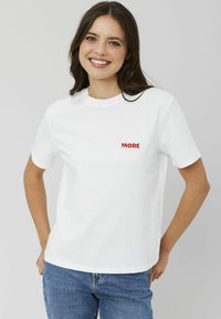 T-shirt en coton blanc avec un graphique rouge "MORE" sur la zone de la poitrine gauche, à manches courtes et col rond. Design doux et décontracté.