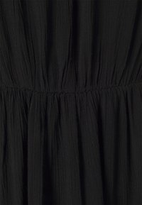 Le tissu de la robe noire présente une surface texturée et froissée avec des sections froncées créant du volume et une apparence douce et fluide.