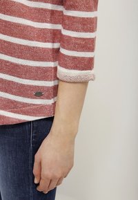 Rood-wit gestreepte longsleeve top met opgerolde mouwen, gemaakt van textuurstof. Bevat een klein merklogo aan de zijkant.