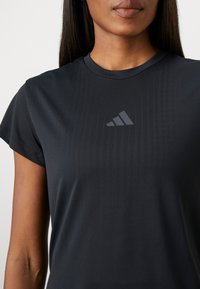 Must kärgvärvi sportpoliester T-särk lühikeste varrukatega, tekstuuriga kangast ja diskreetse peegelduva logoga rinnas. Omab ümmargust kaelust.