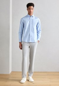 Helleblaue, knöpfbare Hemd mit Kragen; graue, maßgeschneiderte Hose; cremefarbene Sneakers; glatte Stofftexturen, moderner Schnitt.