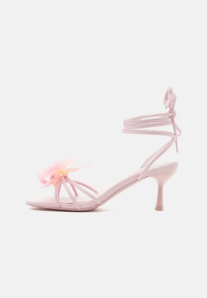 Sandale cu toc înalt, cu barete roz deschis, cu înfăşurare în jurul gleznei şi floare decorativă roz pe bareta frontală, văzută din profil lateral.