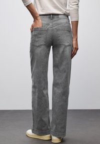 Jeans grigi con una vestibilità rilassata, design a cinque tasche e texture in denim. Presentano una vita a media altezza e gambe dritte, abbinati a scarpe di colore chiaro.
