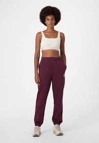 Ljusbeige croptop med figurnära design och randigt band. Vinröda sweatpants med elastiska muddar och sidofickor. Beigemålade sneakers.