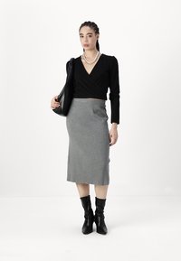 Zwarte wikkel-top, grijze gebreide kokerrok en knie-hoge zwarte laarzen; model met een zwarte handtas, met gevlochten haar en een gelaagde ketting.