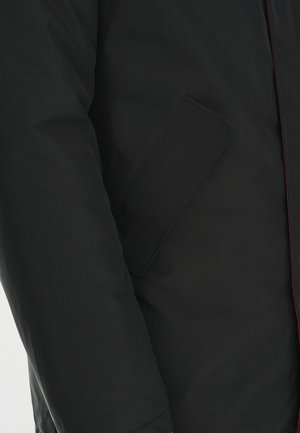 Czarna ocieplana kurtka o gładkim wykończeniu, z boczną kieszenią i kontrastowym czerwonym przeszyciem wzdłuż zamka. Prosty design, bez ozdób.