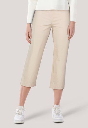 Beige cropped Hosen aus leichtem Stoff mit geradem Bein und einem Saum knapp unterhalb des Knies, kombiniert mit weißen Sneakers.