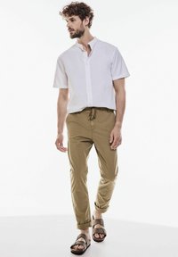 Vit kortärmad skjorta med knappslå, khaki-byxor med dragsko och bruna platta sandaler har en avslappnad design och en figurnära silhuett.