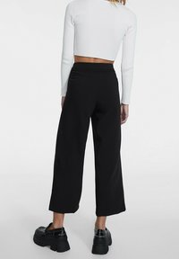 Zwarte wijde broek met hoge taille en een gladde textuur, gecombineerd met stevige zwarte plateau schoenen voor extra hoogte.