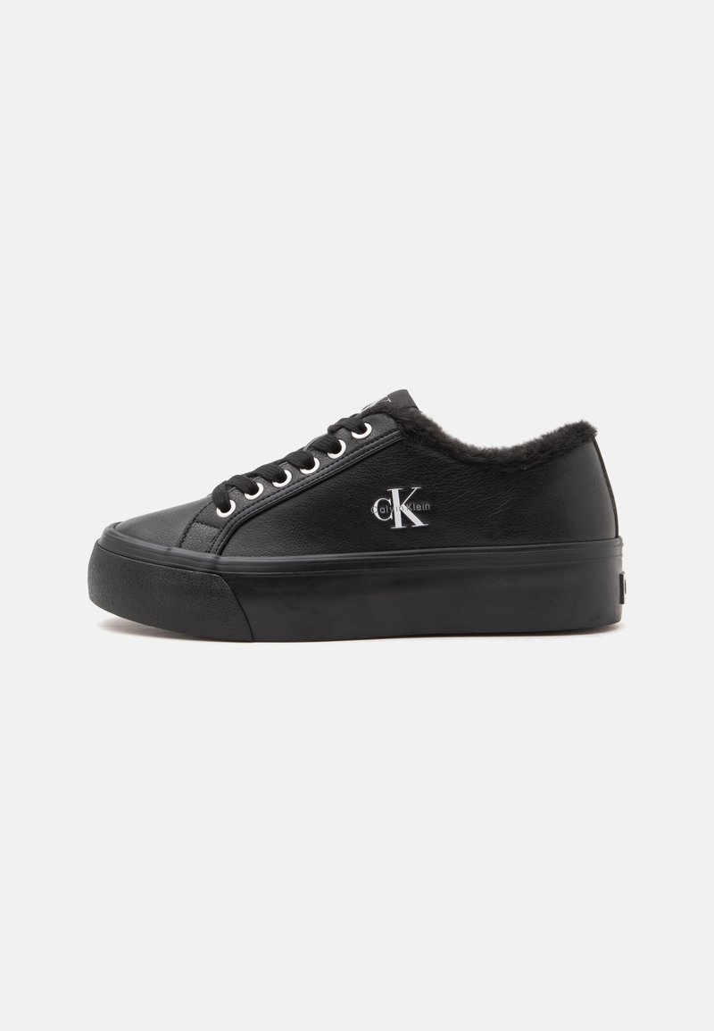 Baskets basses en cuir noir avec lacets, semelle épaisse, doublure en fourrure et logo Calvin Klein sur le côté.