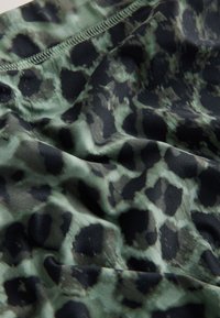 Tissu à imprimé léopard vert et noir avec des coutures visibles et des plis naturels créant texture et ombres.