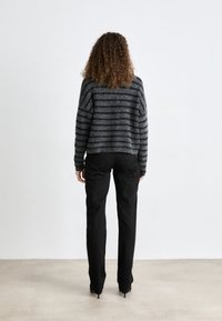 Suéter gris a rayas de gran tamaño, hecho de material suave, combinado con pantalones negro ajustados y zapatos de tacón alto, visto desde atrás.