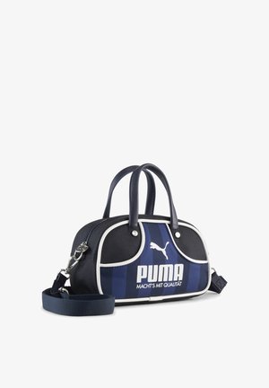 Kompaktna ručna torba marke Puma u mornarsko plavoj i crnoj boji s bijelim obrubom, dvostrukim ručkama, odvojivim remenom za nošenje preko ramena te logotipom i natpisom Puma na prugastom prednjem panelu.