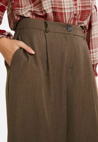 Bruine op maat gemaakte broek met een gladde textuur, voorzien van een voorplooi, zijzakken en een enkele knoopsluiting in de taille.